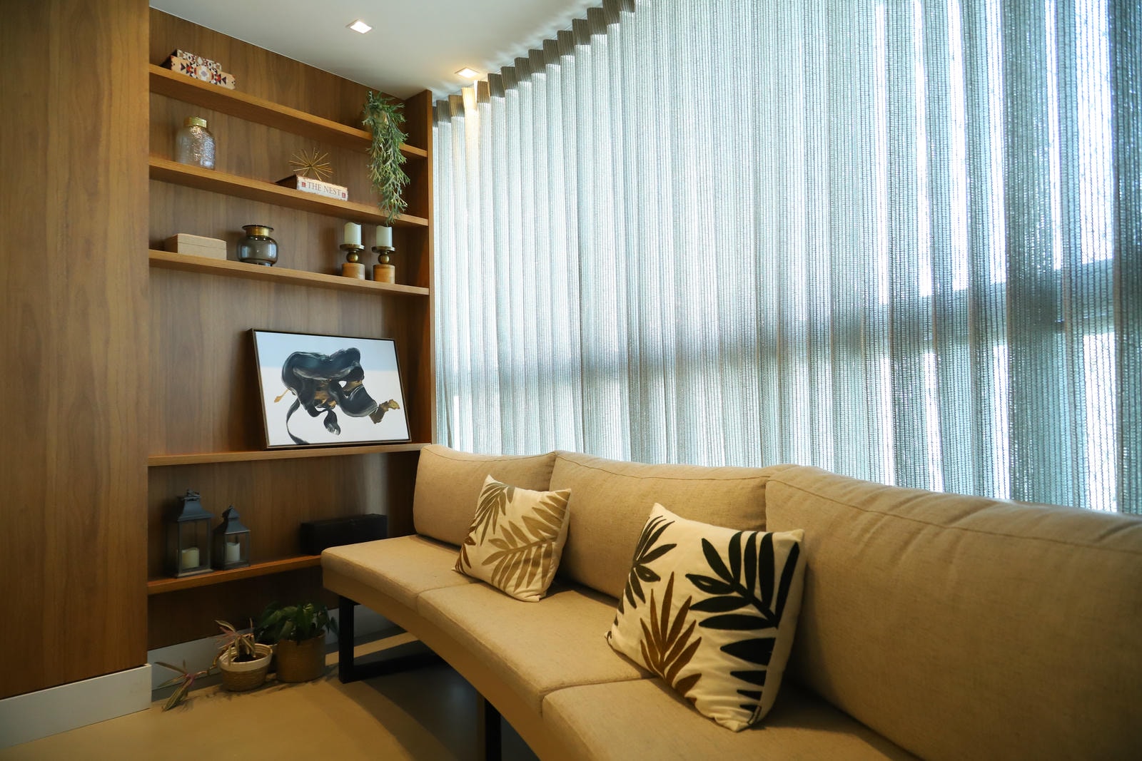 Sala de estar com sofá bege, estante de madeira e cortinas claras